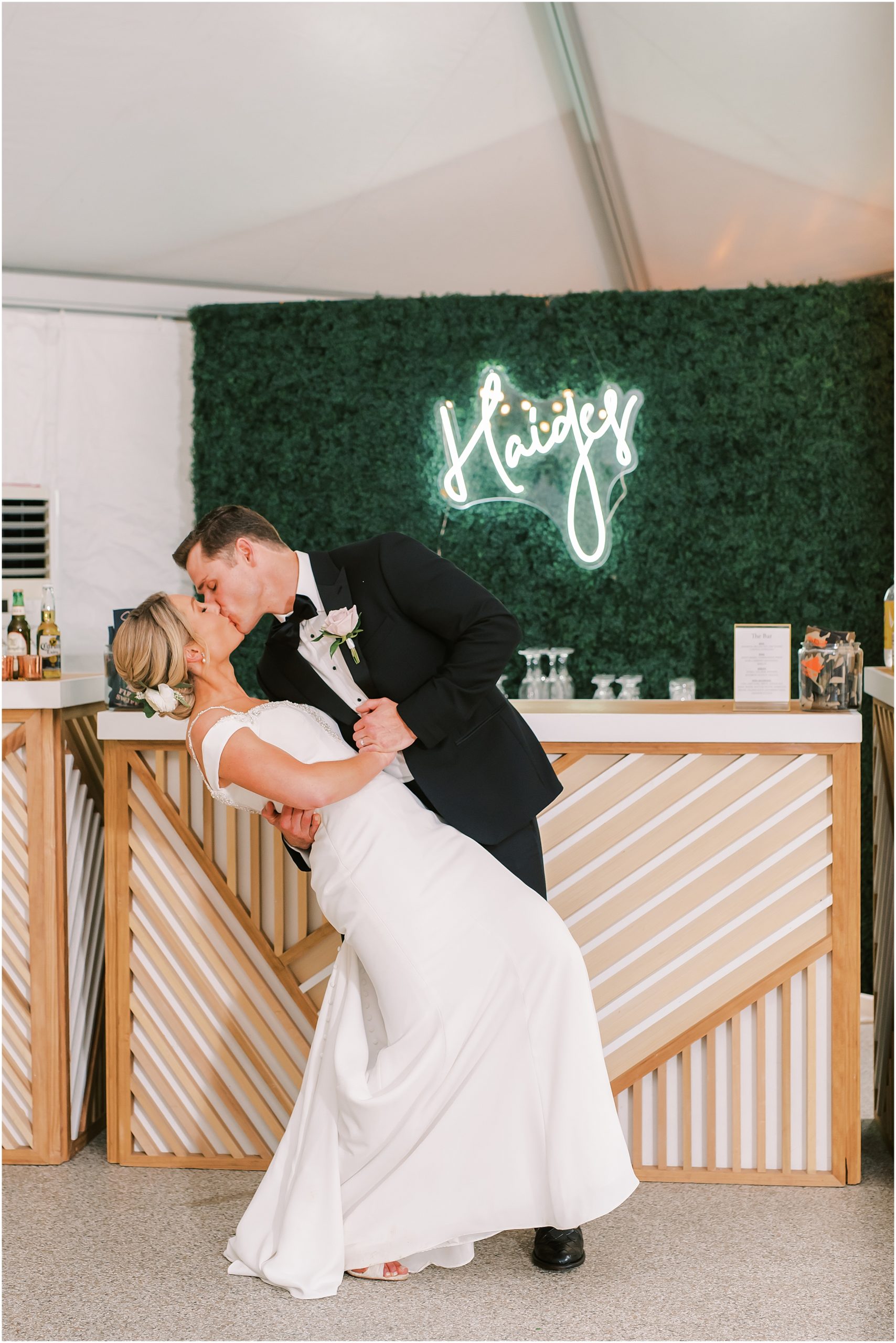 Bride and groom kiss in front of custom neon wedding sign